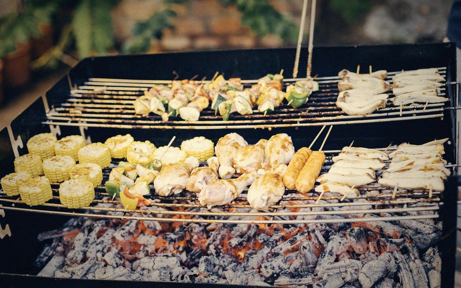 Corn cobs, chicken pieces, skewers and sausages cooking on a charcoal barbecue grill
