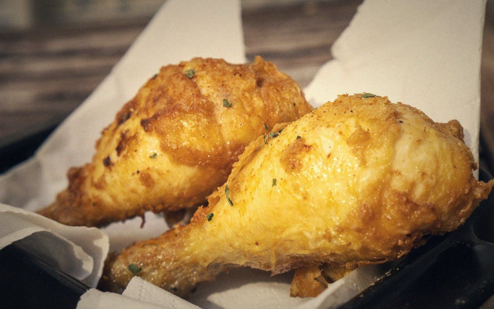 Two golden fried chicken drumsticks resting on paper liner in a black basket