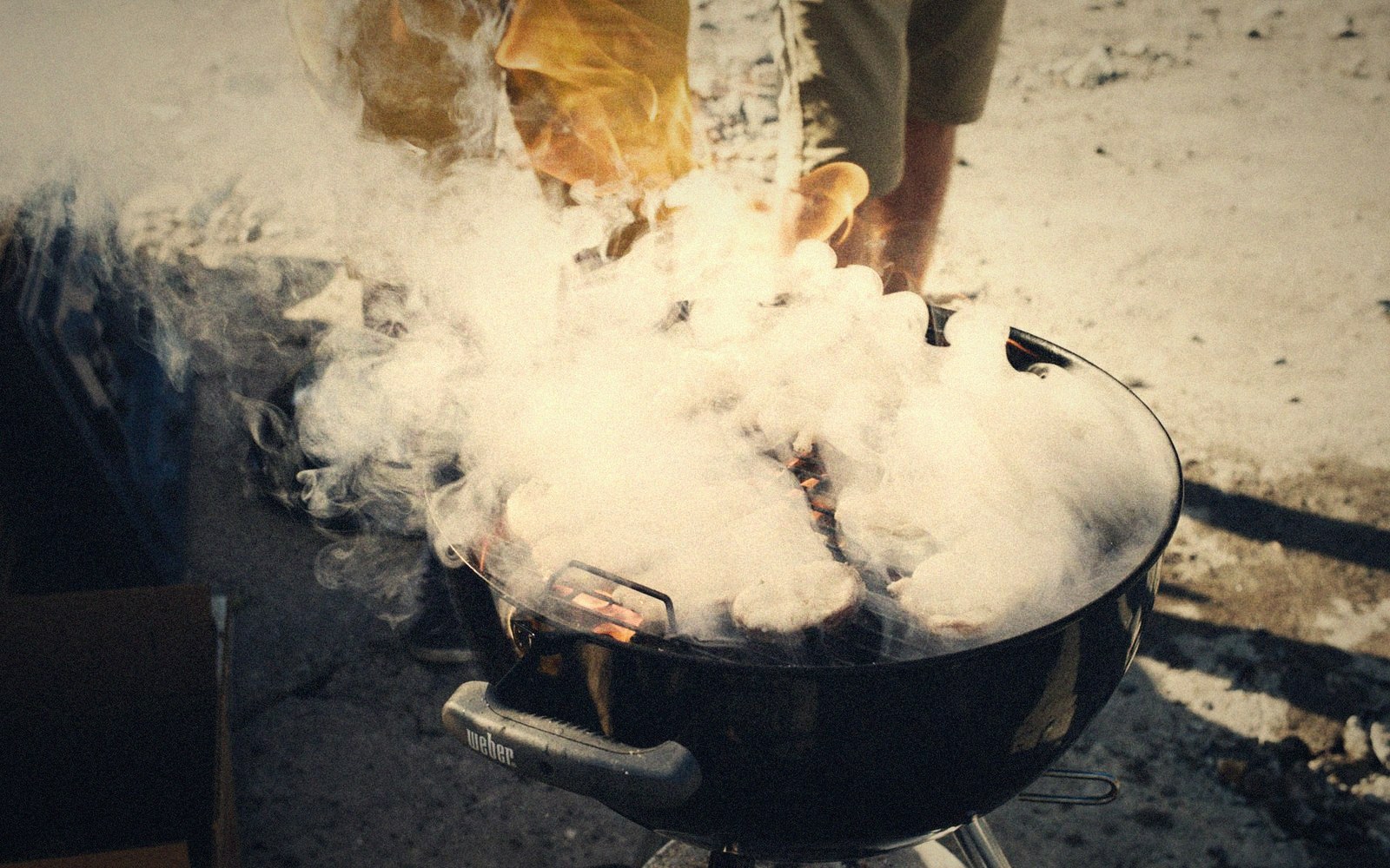 Thick smoke billows from a charcoal-filled Weber kettle grill outdoors