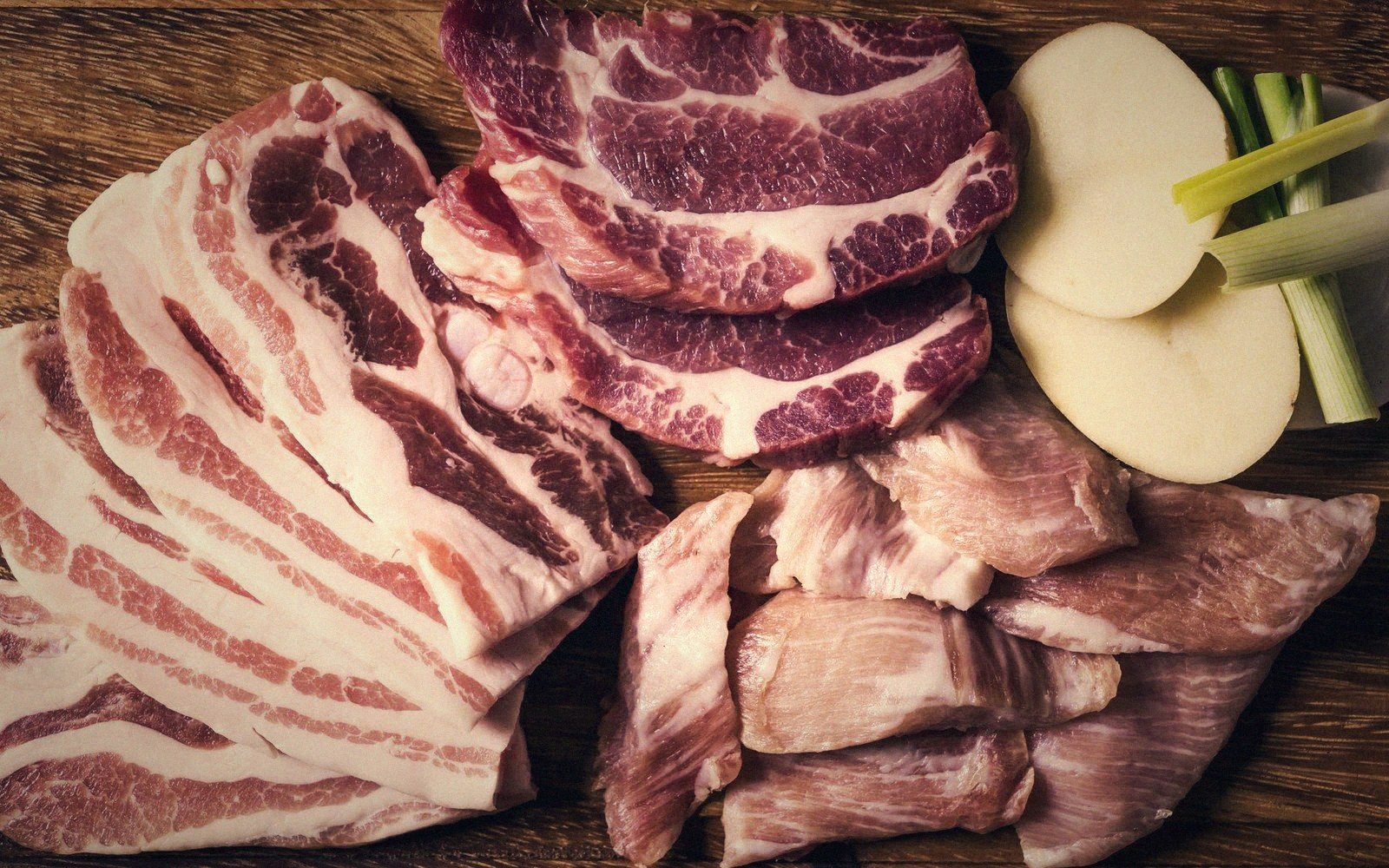 Sliced pork belly, shoulder steaks, and tripe arranged with potato slices and scallions
