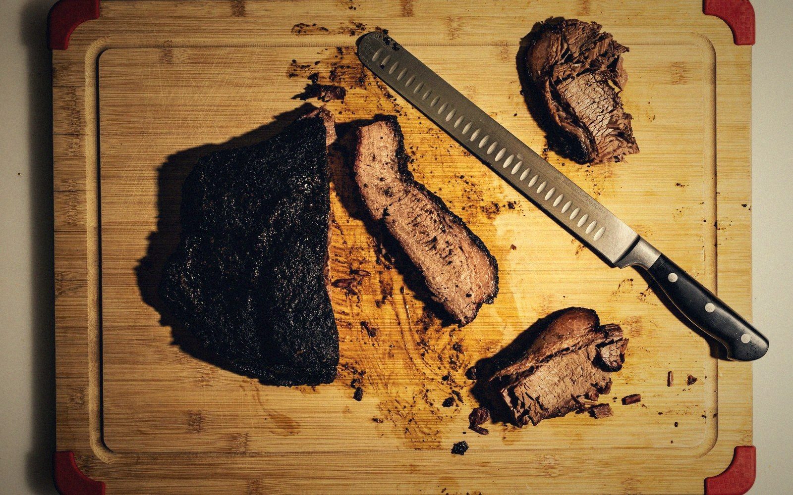 Sliced smoked brisket with dark bark rests beside a carving knife on a cutting board