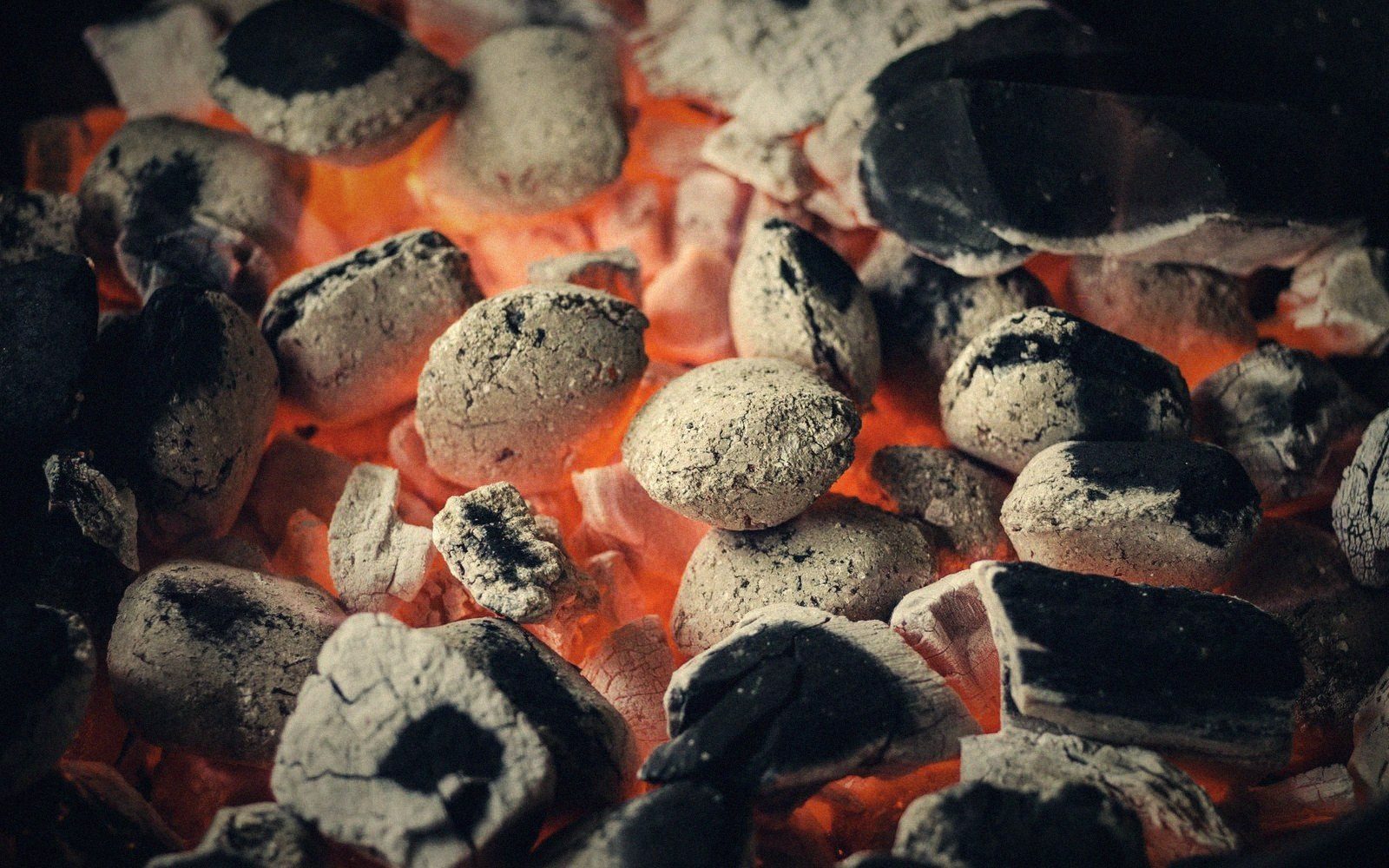 Close-up of glowing charcoal briquettes covered in white ash, embers burning beneath