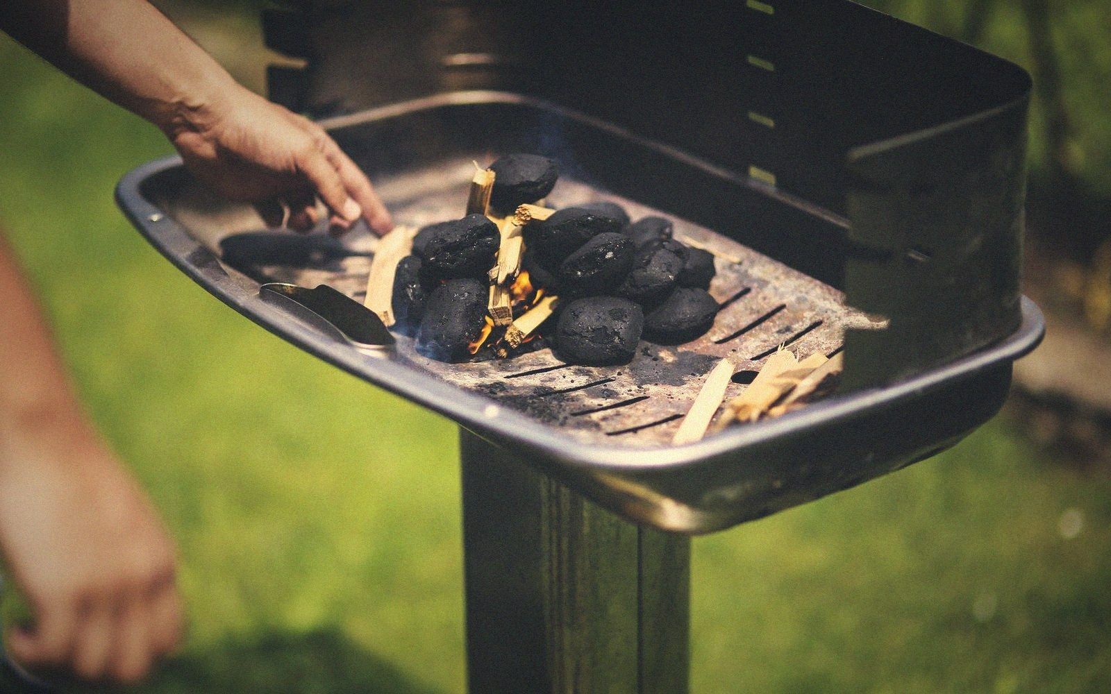 A hand arranges wood chips and kindling among charcoal briquettes on an outdoor grill