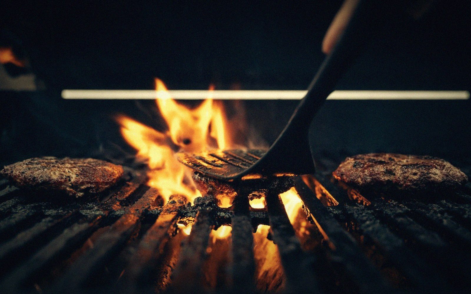 A hand turning one burger with a thin spatula
